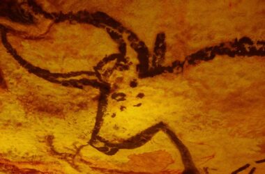 Imagem de uma pintura rupestre pré-histórica em uma caverna, representando um boi. A pintura é feita em tons de vermelho e preto, indicando o uso de materiais naturais como carvão e argila.