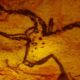 Imagem de uma pintura rupestre pré-histórica em uma caverna, representando um boi. A pintura é feita em tons de vermelho e preto, indicando o uso de materiais naturais como carvão e argila.